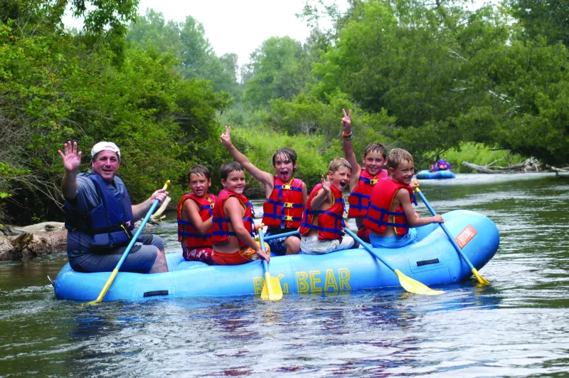 A group of kids and one adult floating on a raft down the Sturgeon River in Indian River, Michigan.