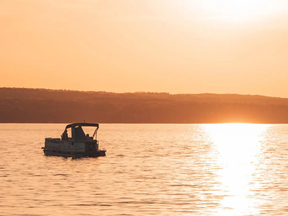 A pontoon boat floats on Burt Lake at sunset.