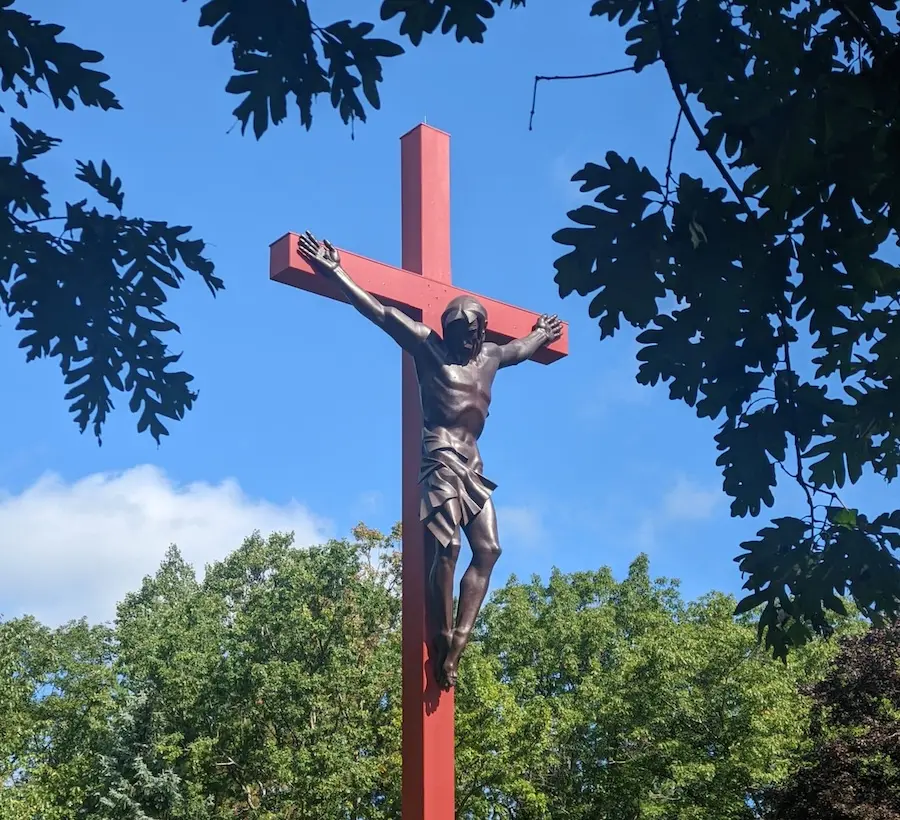 A large crucifix towers over the people and buildings surrounding it.