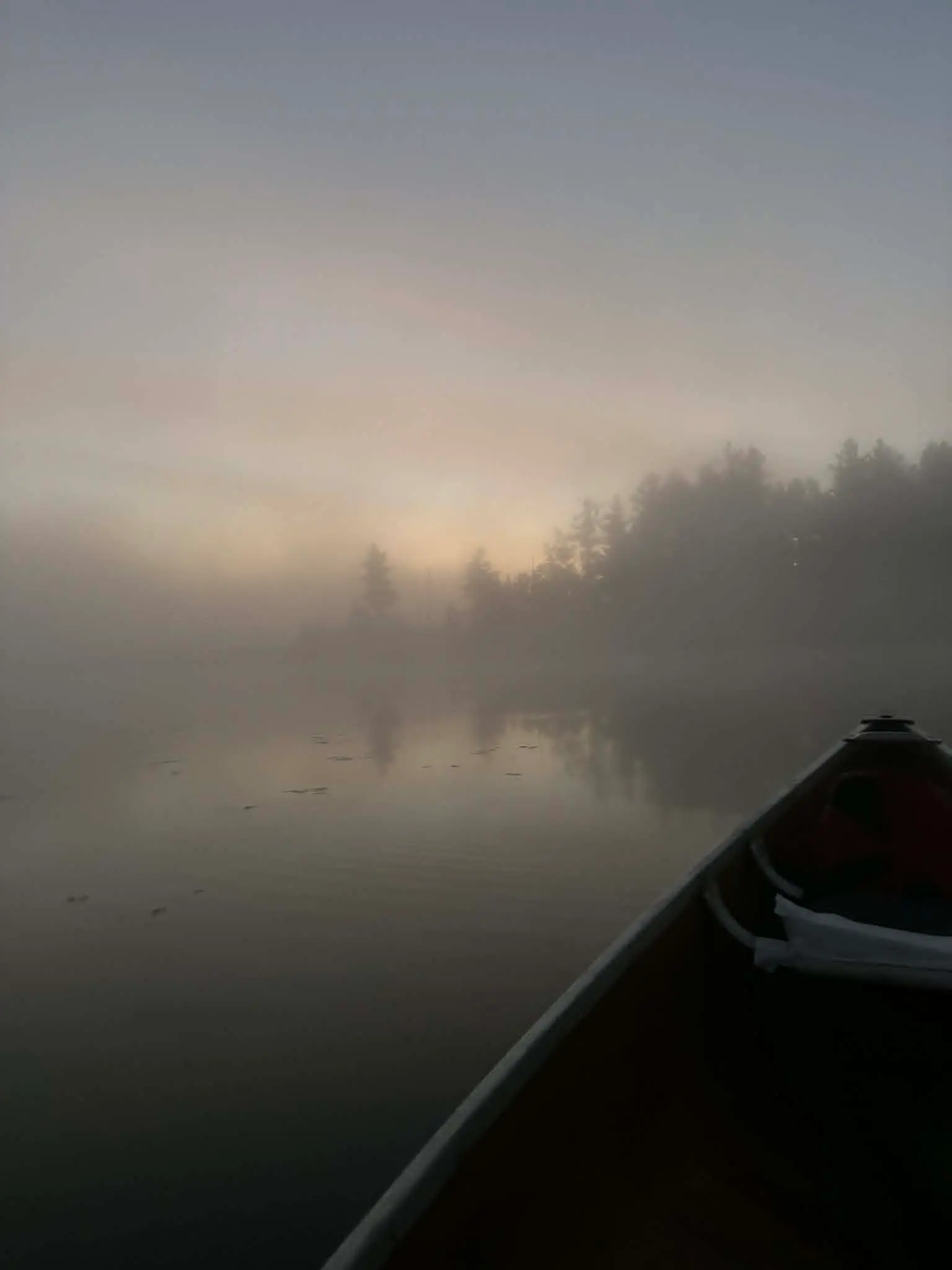 A kayak sitting on an open body of water with fog encapsulating the scene.
