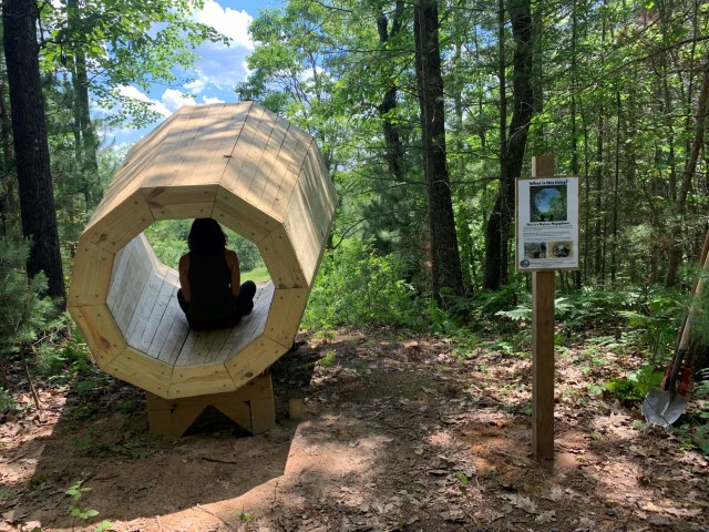 A child sitting in the Nature Megaphone overlooking a lush green Pigeon River Valley at the Boyd Banwell Nature Preserve.