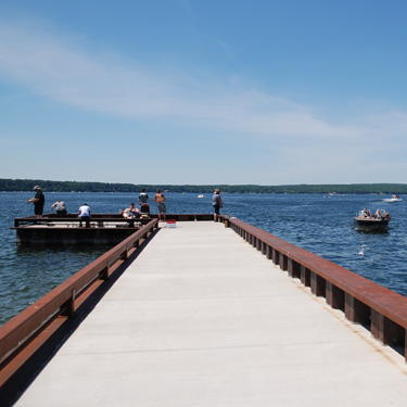 A large paved fishing pier jutting out into Burt Lake.