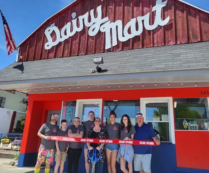 A group of people smiling and holding a red ribbon in front of the Dairy Mart in Downtown Indian River.