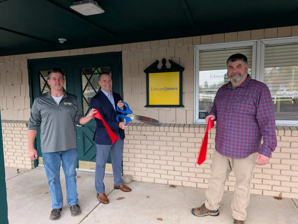 A group of people smiling and holding a ribbon in front of the Edward Jones office in Downtown Indian River.