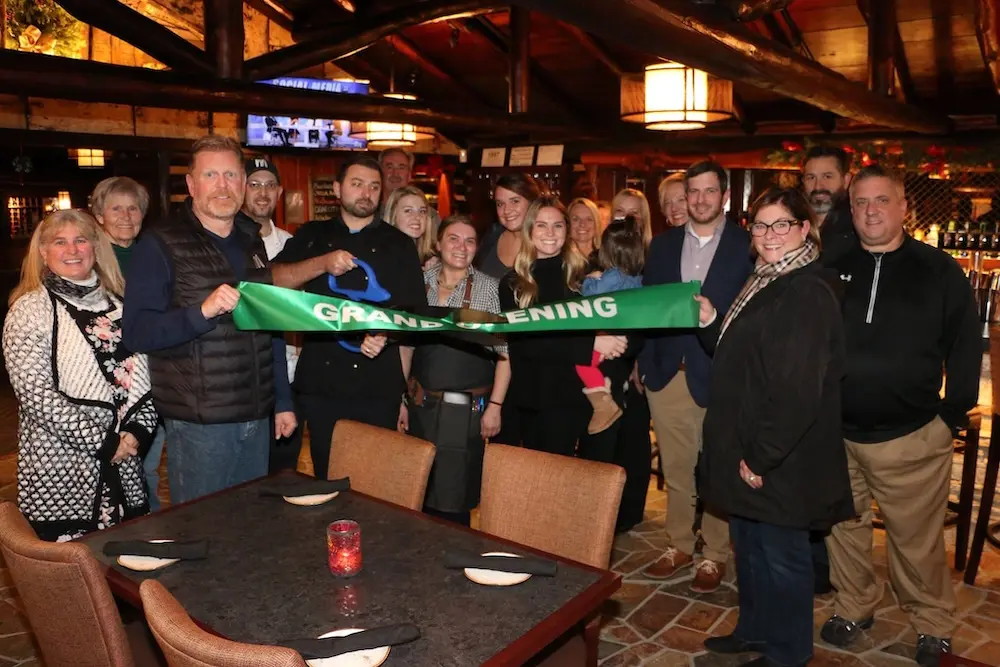 A group of people smiling and holding a ribbon at Michael's Tavern.