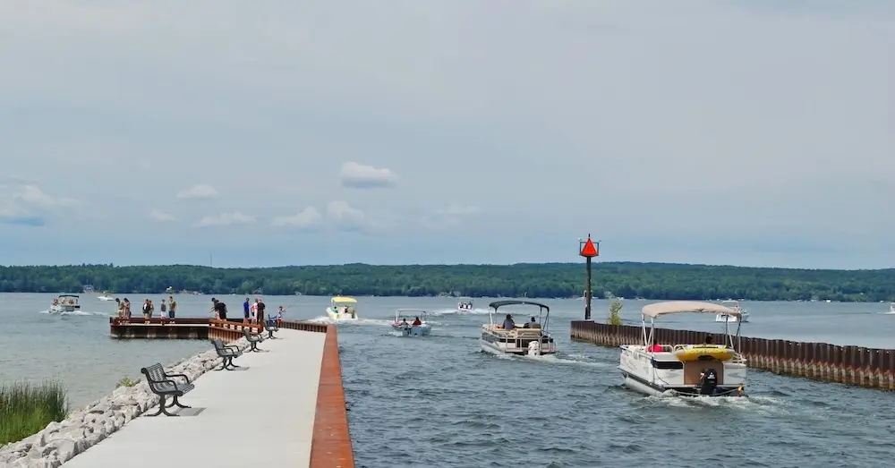 People stand along Veteran's Fishing Pier at Devoe Beach in Downtown Indian River. Boaters ride along the Indian River heading into Burt Lake. Beachgoers swim in the water along the opposite of the pier.