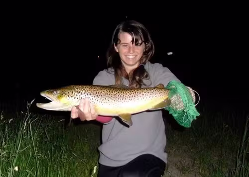 Amanda Monthei smiling and holding a large brown trout in the pitch dark.