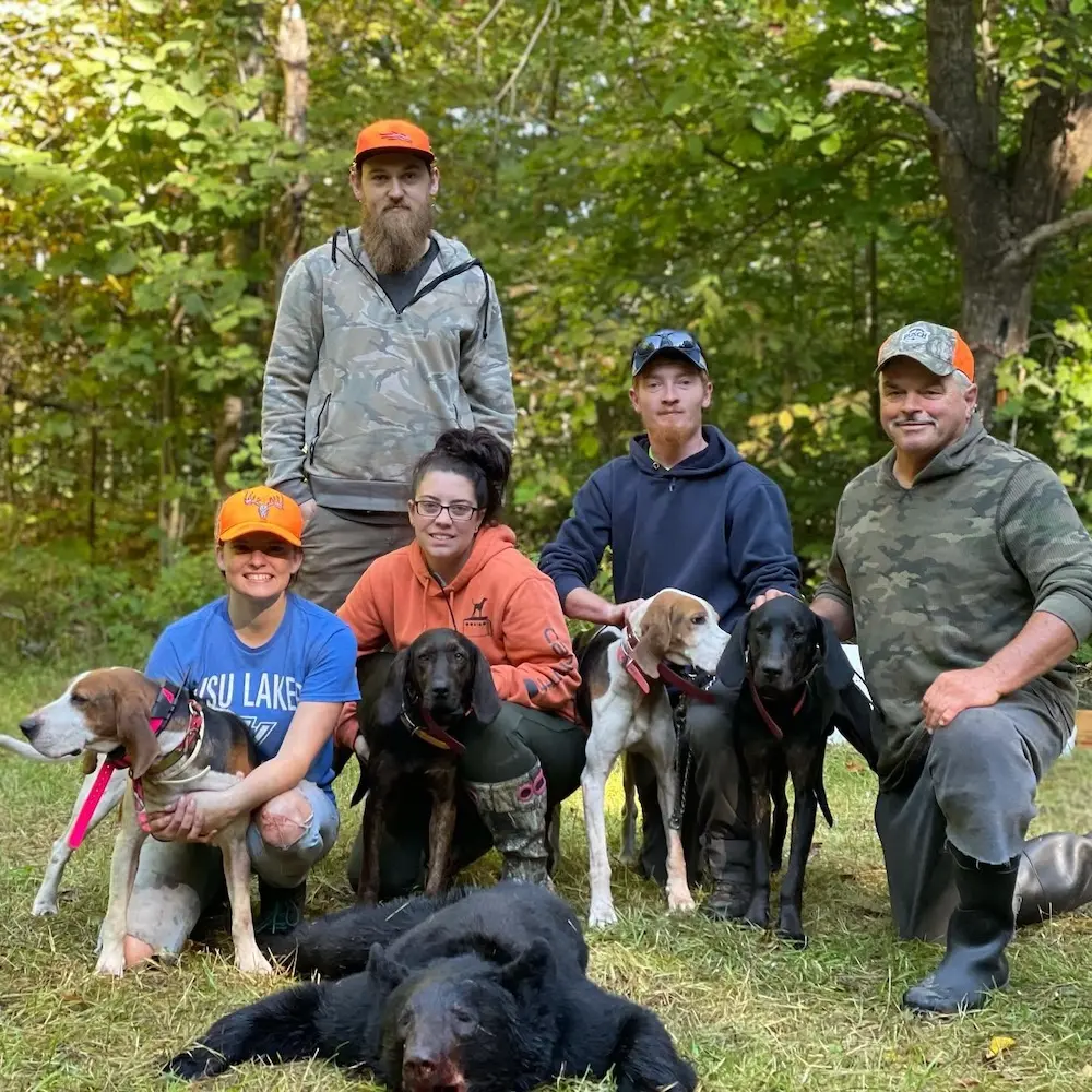 A group of bear hunters stand posing with the bear they harvested with their bear hounds standing proudly with them.